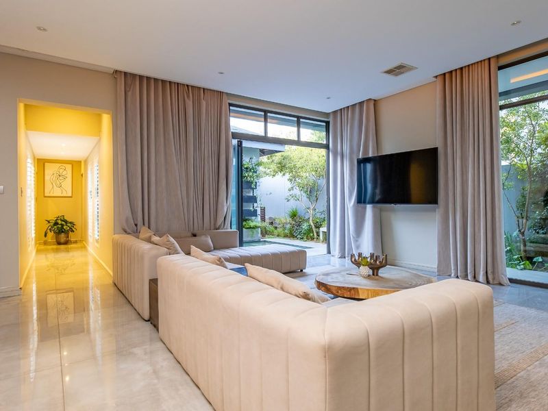 Modern living room featuring large format floor tiles, recessed lighting, and floor-to-ceiling glass doors providing seamless access to the outdoor garden area.