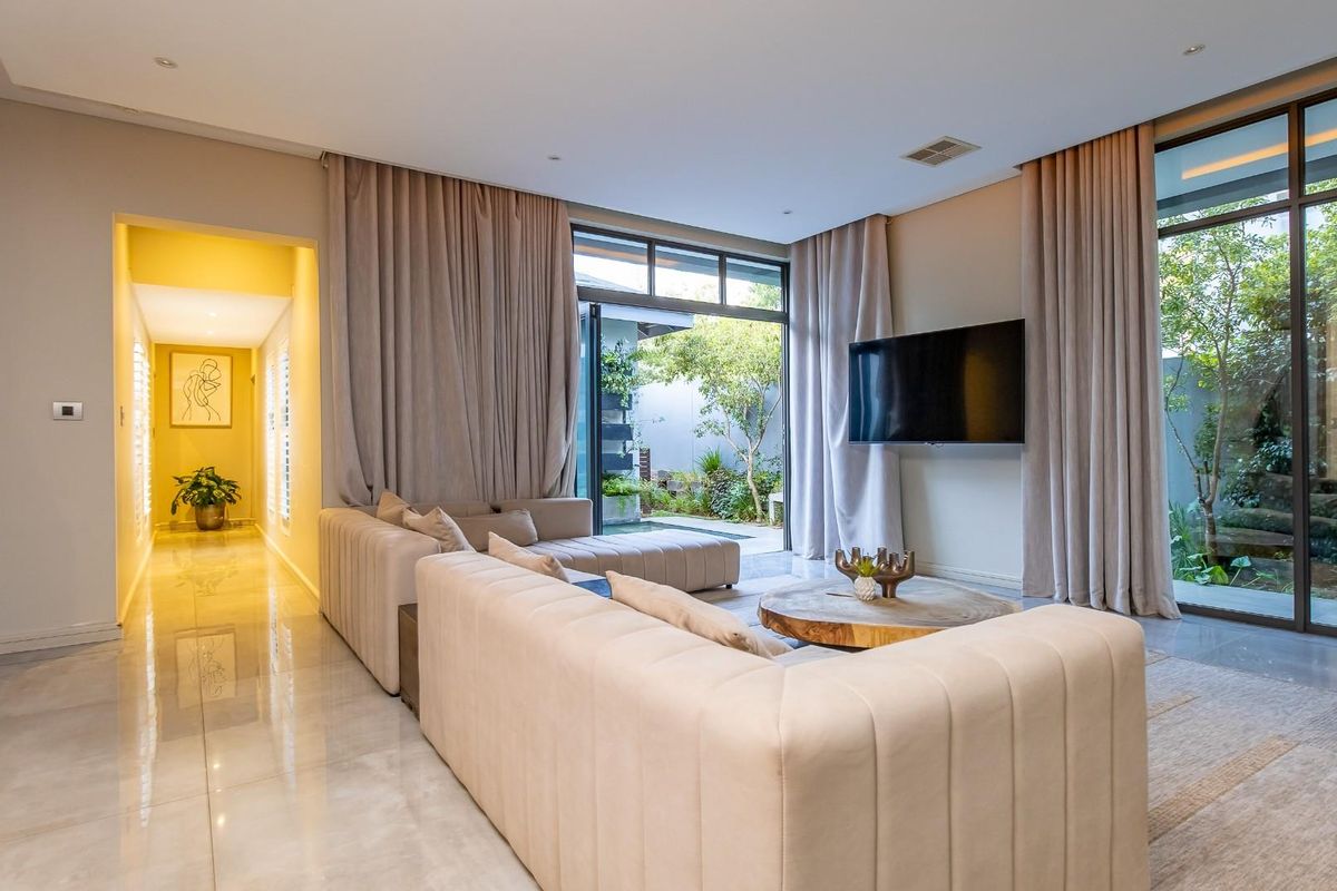 Modern living room featuring large format floor tiles, recessed lighting, and floor-to-ceiling glass doors providing seamless access to the outdoor garden area.