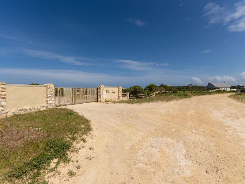 Entrance view of the vacant residential property featuring a gated access point with stone masonry pillars and an unpaved road.