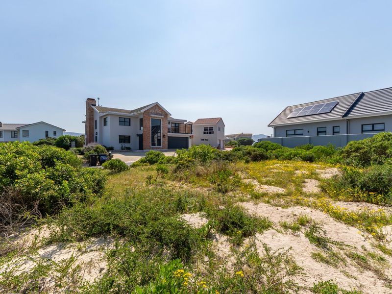 A view of a vacant residential plot featuring natural sand dunes and coastal vegetation, situated within a developed neighborhood.