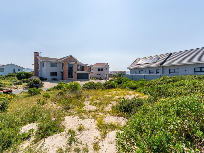 A view of a vacant residential plot featuring natural sand dunes and coastal vegetation, situated in a developed neighborhood.