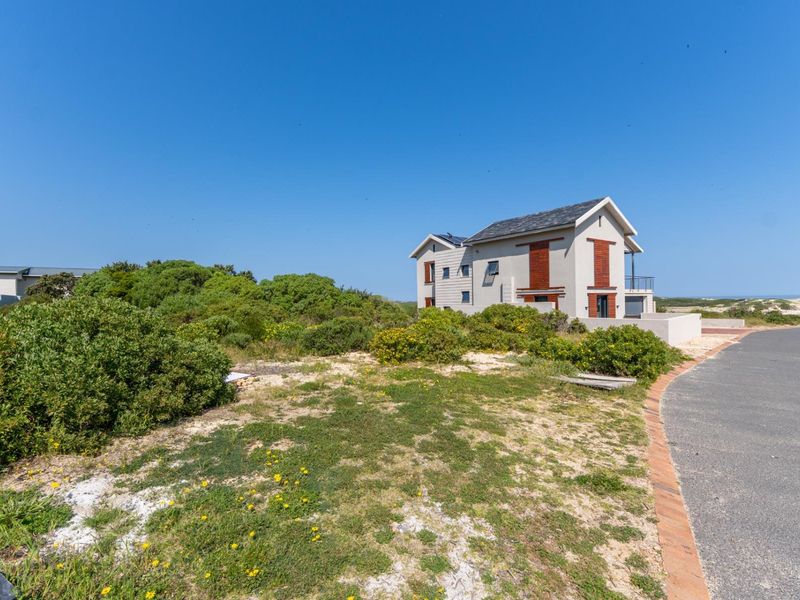 A view of a residential property from the street, featuring a paved driveway and surrounding coastal vegetation.