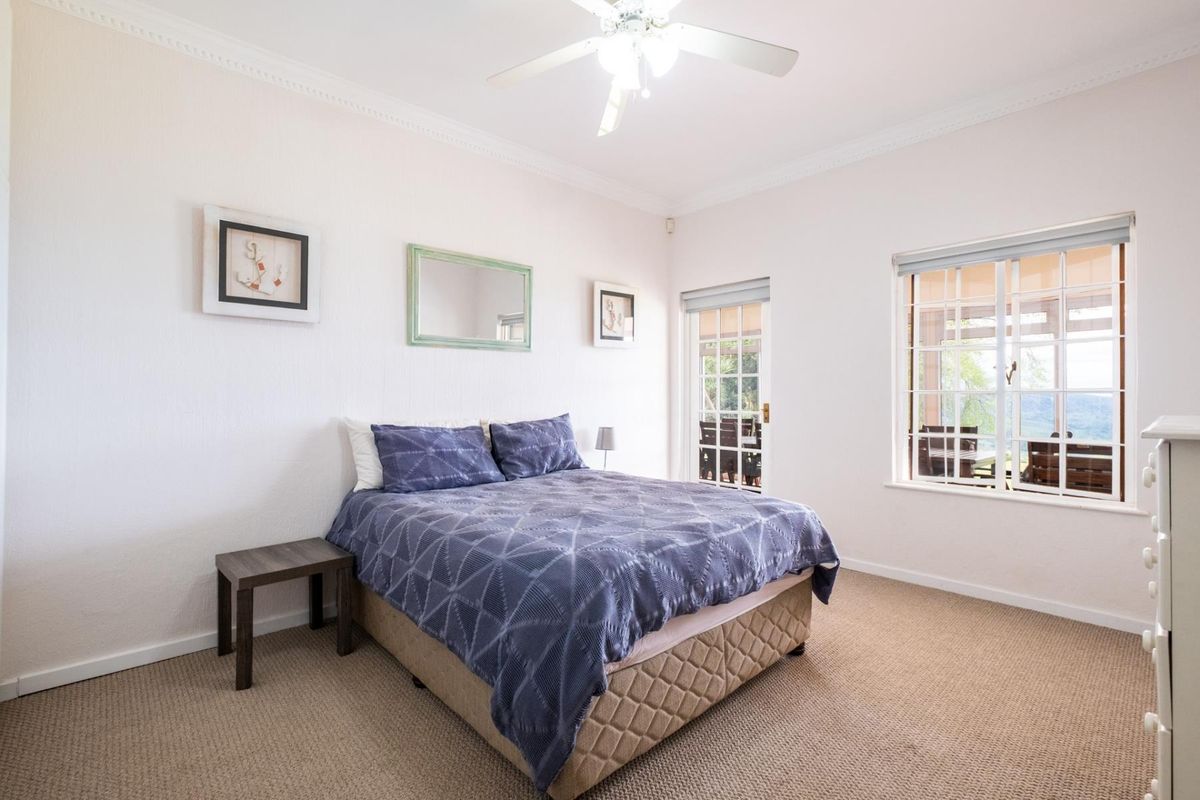 A well-lit bedroom featuring neutral walls, carpeted flooring, a ceiling fan, and direct access to an outdoor area through a glass panel door.