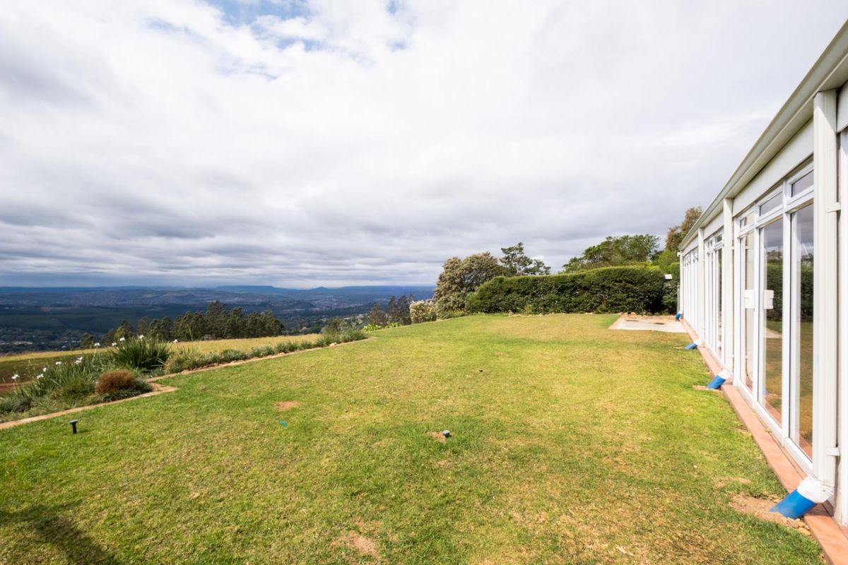 Spacious rear garden featuring a well-maintained lawn, established hedging, and expansive views, with direct access to the home via large sliding glass doors.