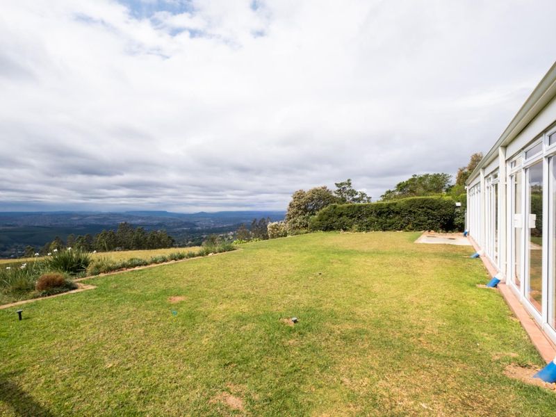 Spacious rear garden featuring a well-maintained lawn, established hedging, and expansive views, with direct access to the home via large sliding glass doors.