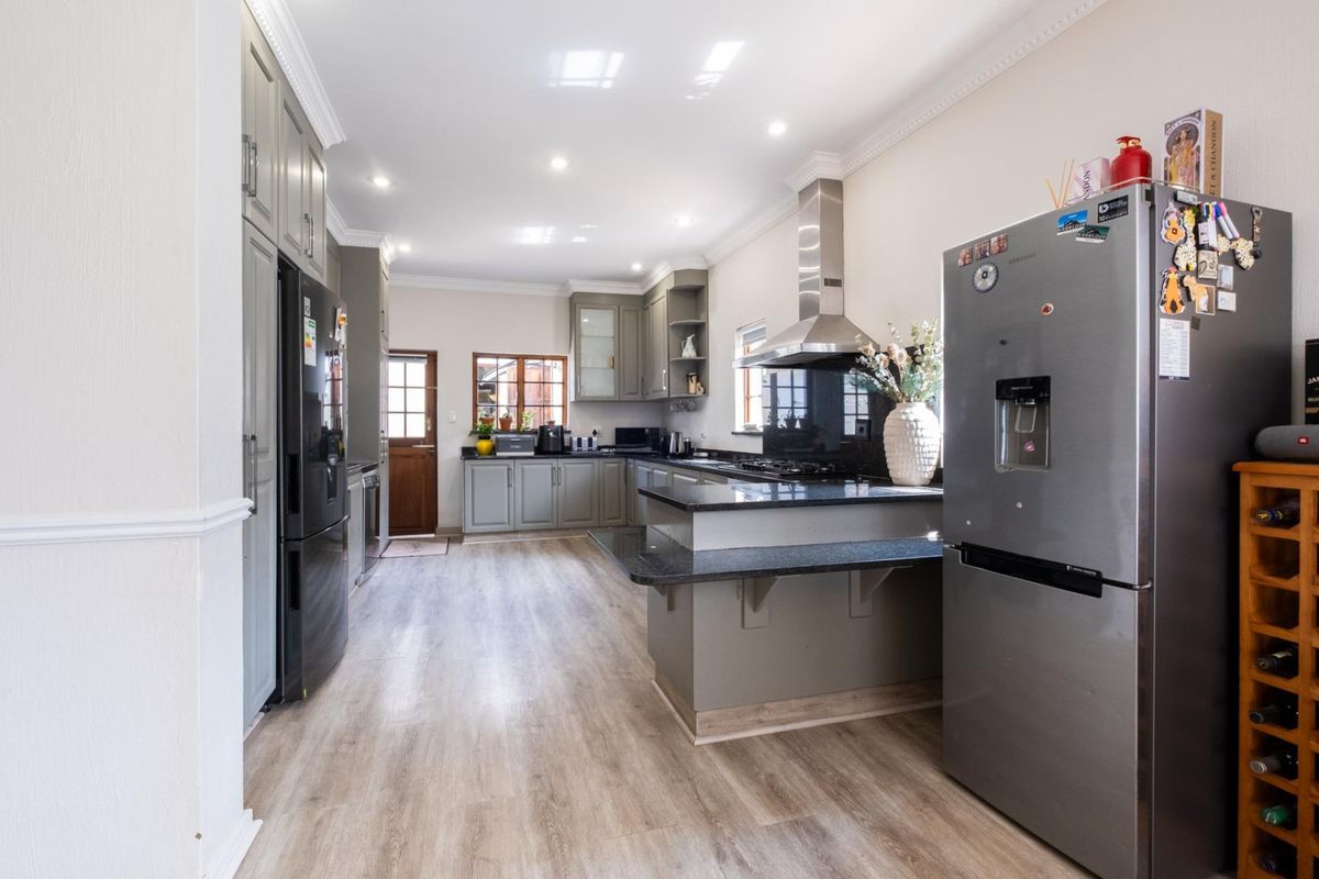 Modern kitchen featuring grey cabinetry, granite countertops, a gas hob with stainless steel extractor, and durable laminate flooring with recessed lighting.