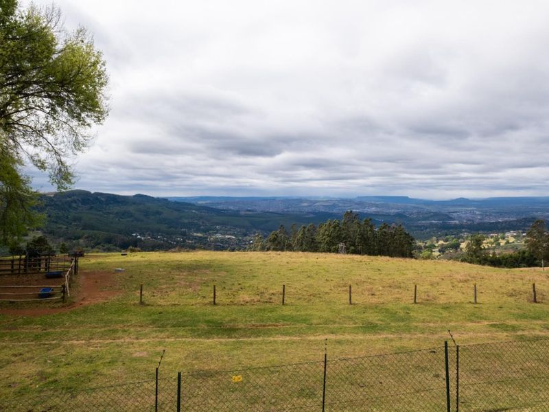 Expansive elevated landscape view overlooking rolling hills and distant valley scenery, featuring rural fencing and open pasture land.