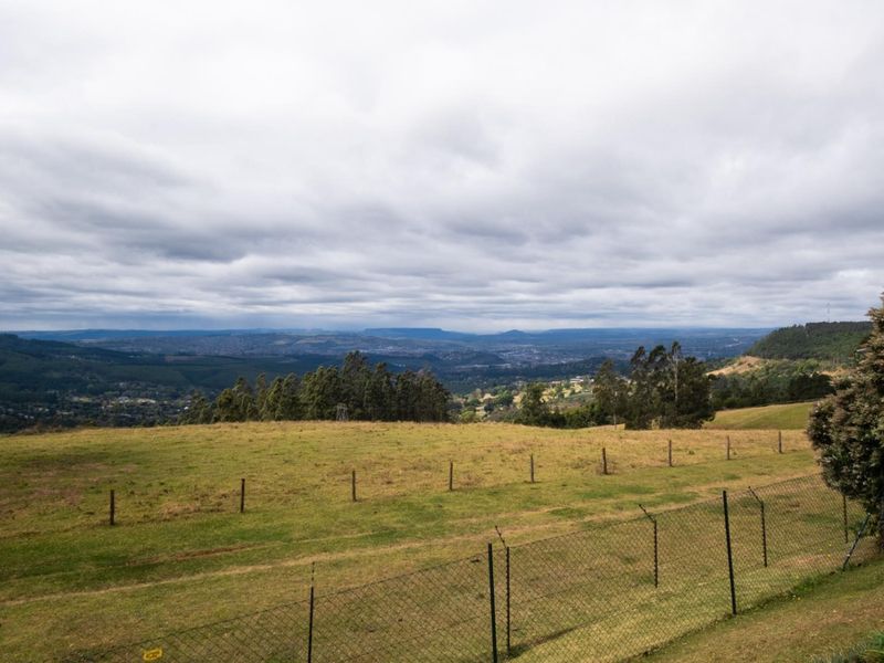 Expansive elevated landscape view overlooking rolling hills and distant valley scenery, framed by rural wire fencing.