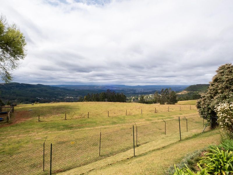Expansive elevated landscape view overlooking rolling hills and valley, featuring perimeter wire mesh and post and rail fencing.