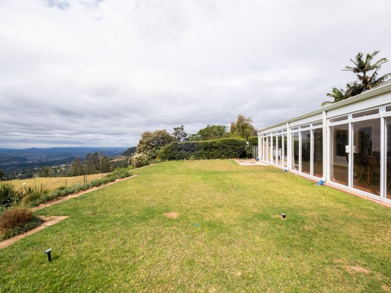 Spacious rear garden featuring a well-maintained lawn, landscaped hedges, and expansive glass sliding doors providing seamless indoor-outdoor flow with panoramic valley views.