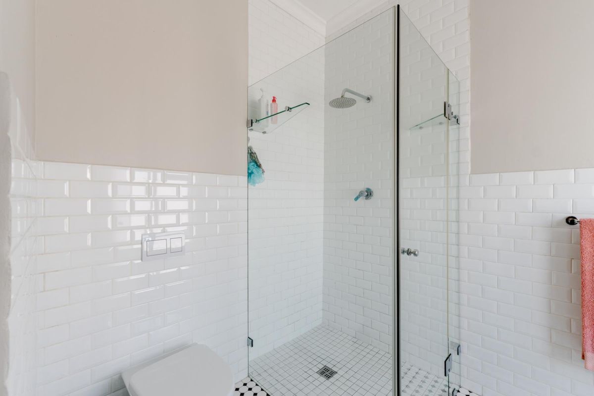Modern bathroom featuring a glass-enclosed walk-in shower with a rain shower head, white subway wall tiles, and classic mosaic floor tiling.