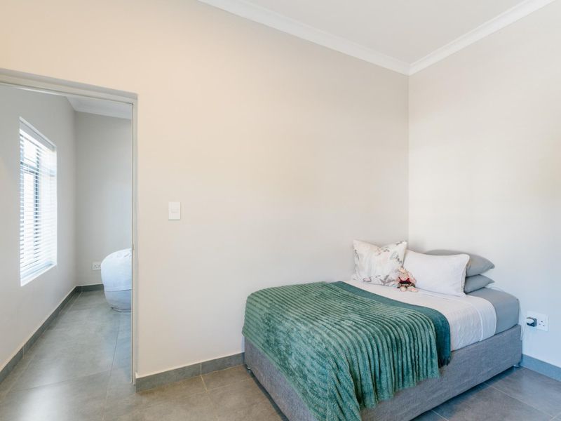 A clean, neutral bedroom featuring tiled flooring, coved cornicing, and a doorway leading to an adjacent room with natural light.