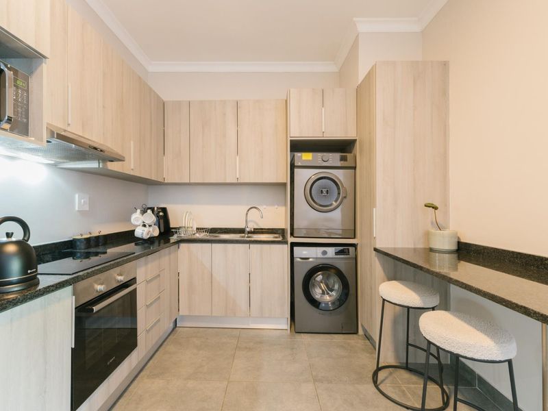 Modern kitchen featuring light wood cabinetry, granite countertops, integrated oven and hob, and a convenient built-in laundry area with a breakfast bar.