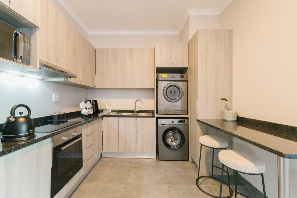Modern kitchen featuring light wood cabinetry, granite countertops, integrated oven and hob, and a convenient built-in laundry area with a breakfast bar.