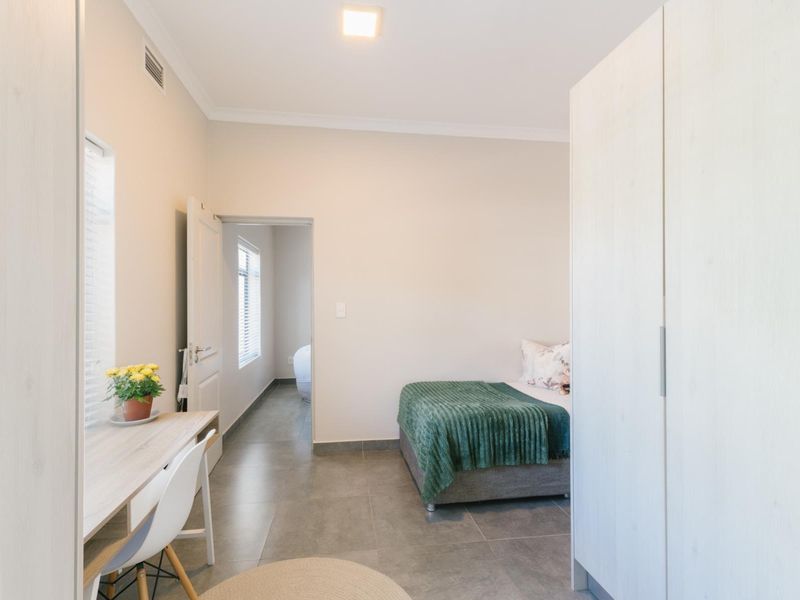 A well-maintained bedroom featuring neutral tiled flooring, built-in cupboards, and recessed lighting, with an adjoining hallway visible.