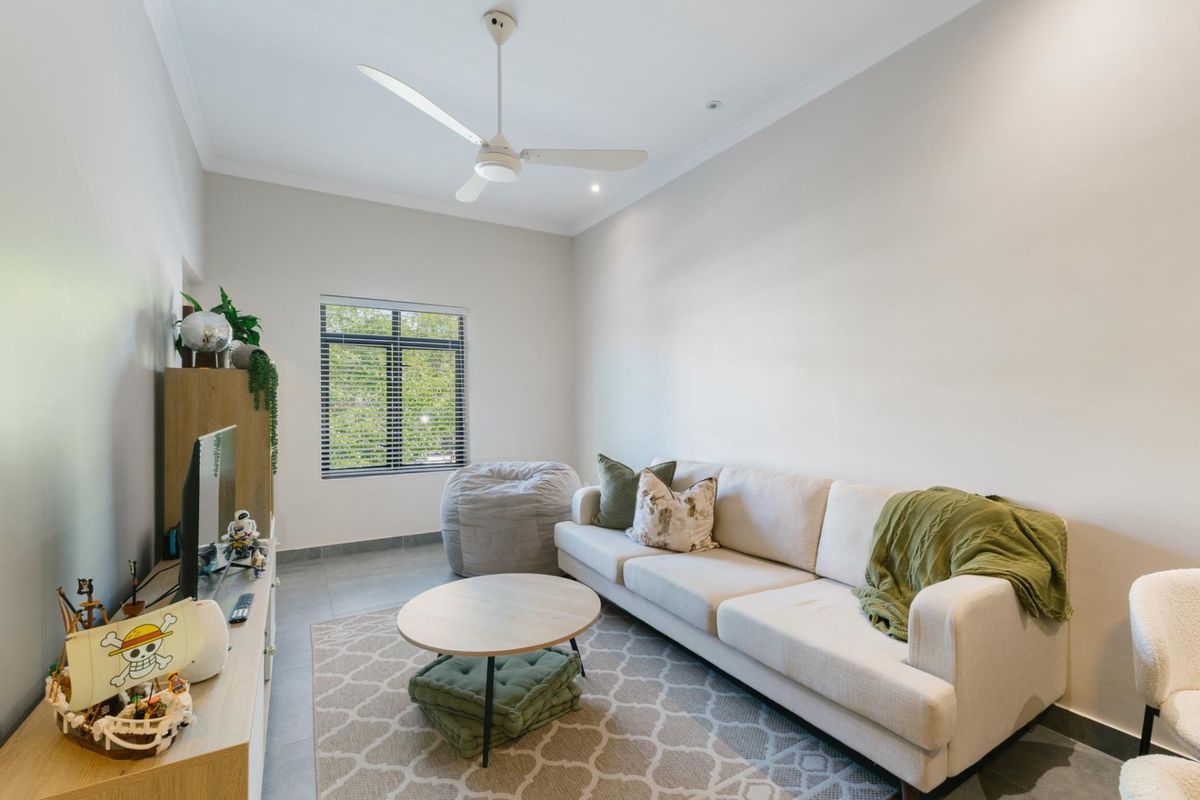 A bright and well-maintained living room featuring tiled flooring, a ceiling fan, and a window with fitted blinds.