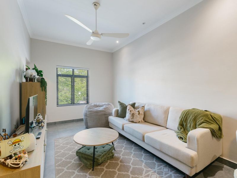 A bright and well-maintained living room featuring tiled flooring, a ceiling fan, and a window with fitted blinds.