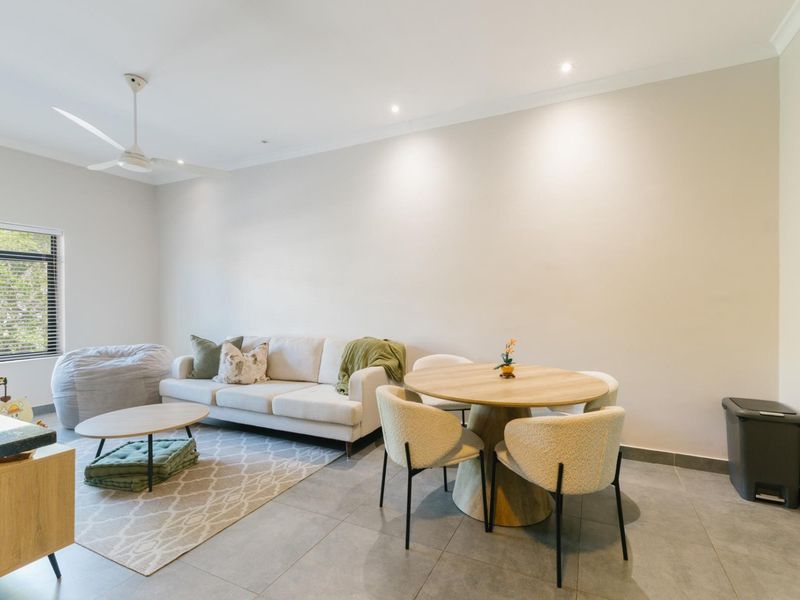 A bright open-plan living and dining area featuring neutral tiled flooring, recessed downlighting, and a modern ceiling fan.