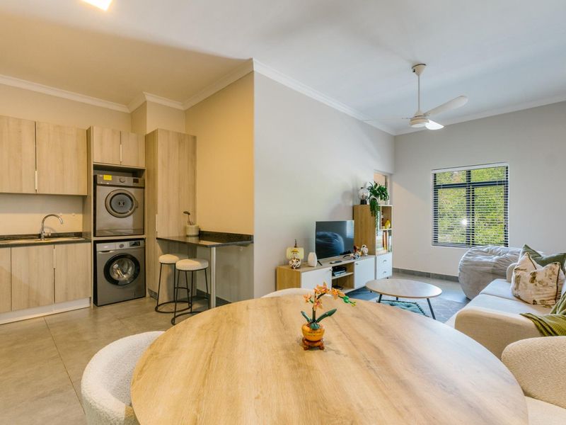 Open-plan living area featuring a compact kitchen with integrated laundry appliances, granite countertops, and tiled flooring, seamlessly flowing into the lounge space.
