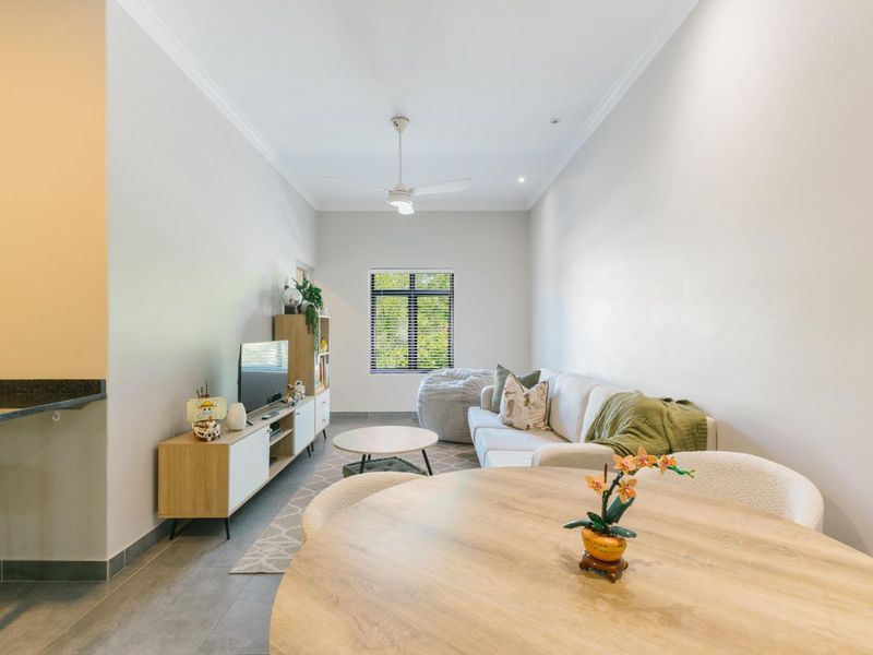 A bright open-plan living and dining area featuring tiled flooring, a ceiling fan, and a breakfast bar, creating a functional and inviting space.