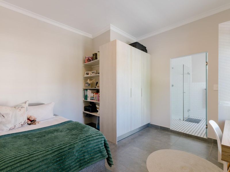 A well-maintained bedroom featuring built-in wardrobes, integrated shelving, tiled flooring, and direct access to an en-suite bathroom.