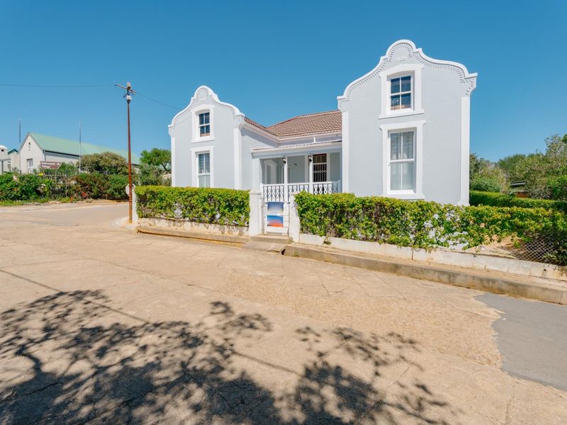 Charming historic house with a distinctive gabled facade, covered front porch, and well-maintained hedged garden boundary.