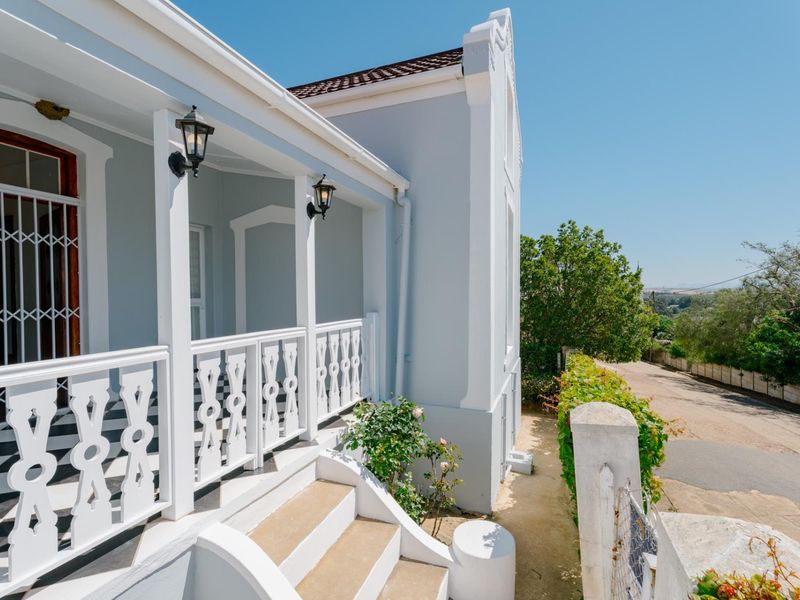 A well-maintained covered veranda featuring decorative white balustrades, exterior lighting, and concrete steps, offering a charming entrance area.