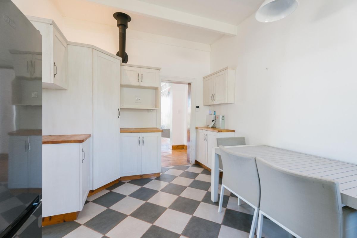 A functional kitchen featuring white built-in cabinetry, wooden countertops, and a distinctive checkered tile floor, with an exposed extractor flue.