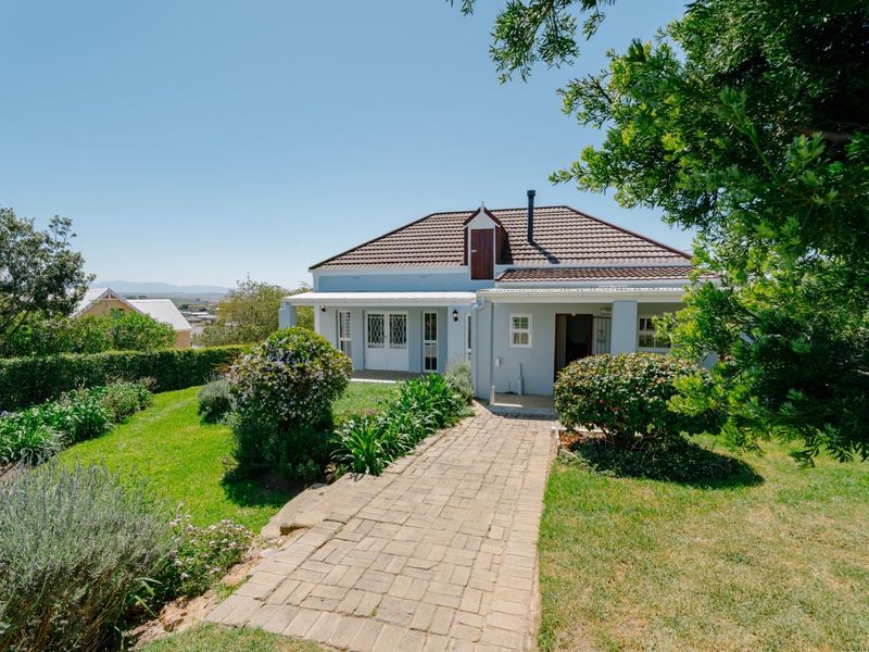 A charming single-story house featuring a tiled roof, a dormer window, and a paved walkway leading to a covered front patio set within a garden.