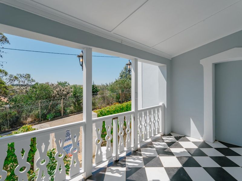 A well-maintained covered balcony featuring classic black and white checkered tile flooring and decorative wooden balustrades with pleasant outdoor views.