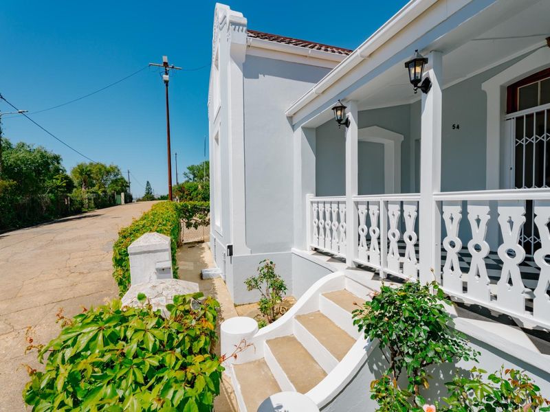 A well-maintained front facade featuring a covered veranda with decorative balustrading, concrete steps, and classic architectural detailing.