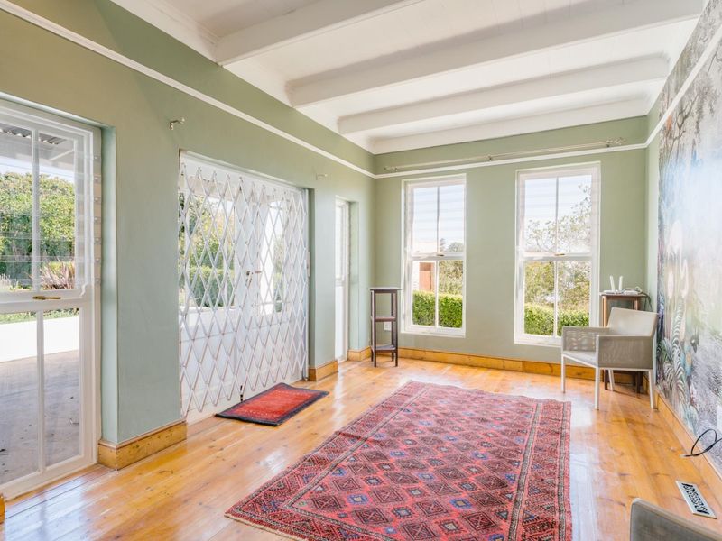 A bright living room featuring exposed timber ceiling beams, polished timber flooring, and large sash windows providing natural light and garden access.