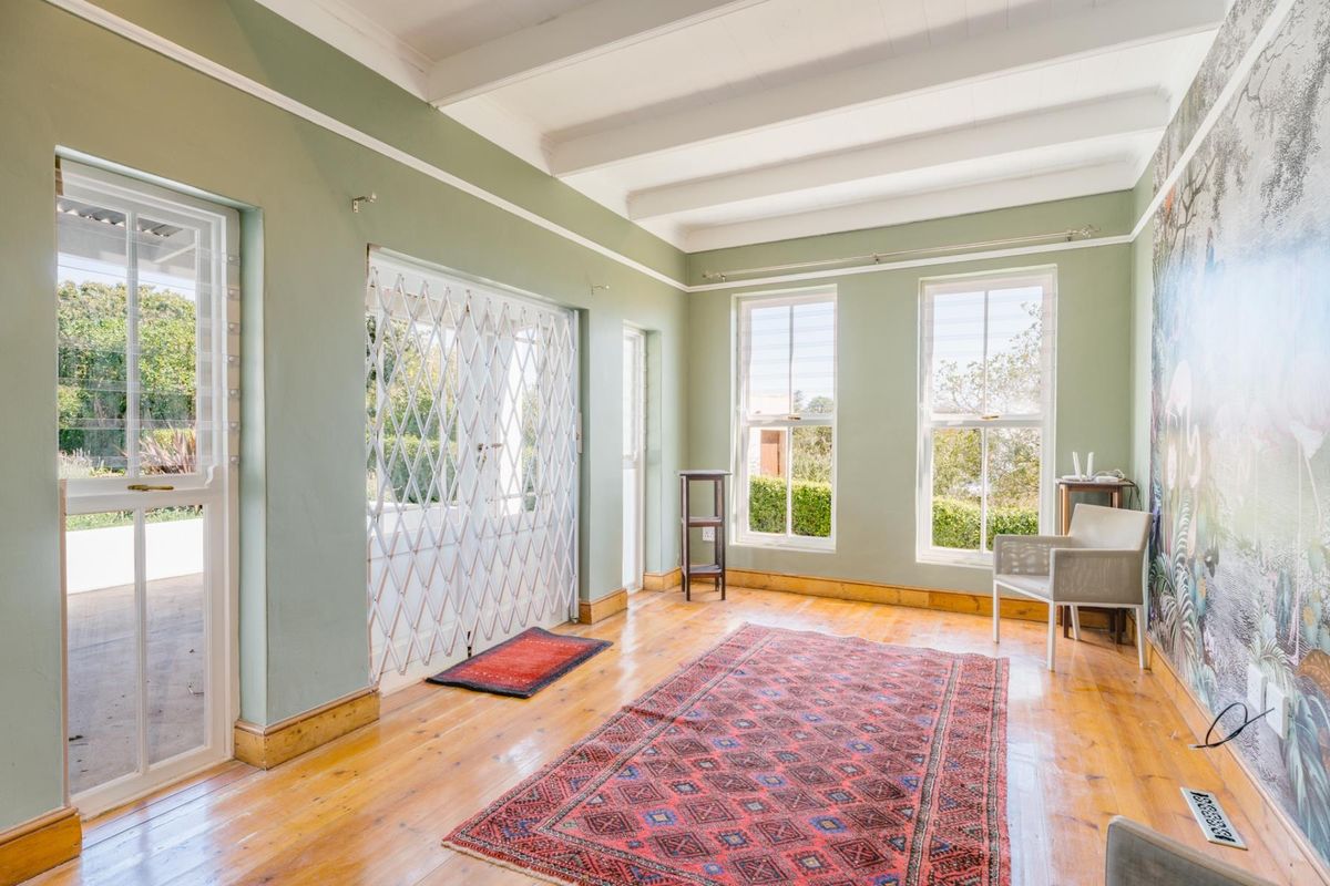 A bright living room featuring exposed timber ceiling beams, polished timber flooring, and large sash windows providing natural light and garden access.