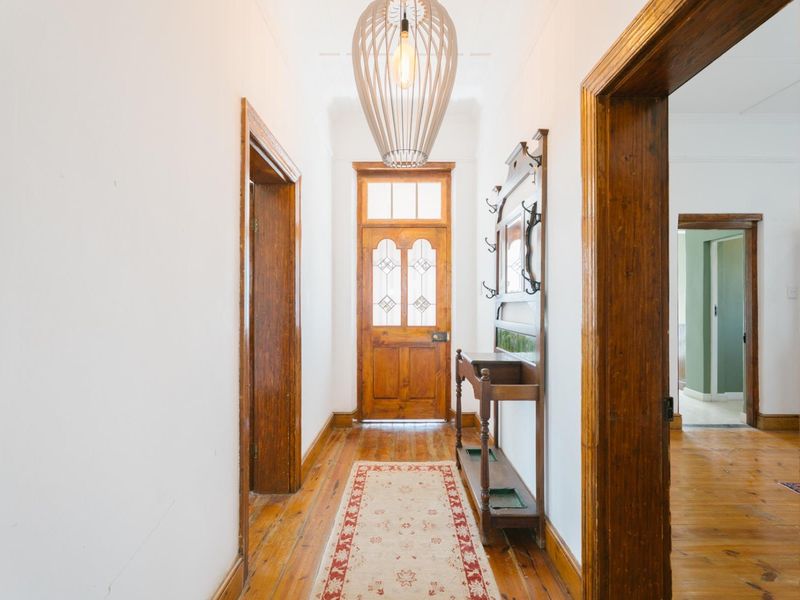A bright, welcoming entrance hallway featuring polished timber flooring, classic wooden door frames, and a decorative leaded glass front door.