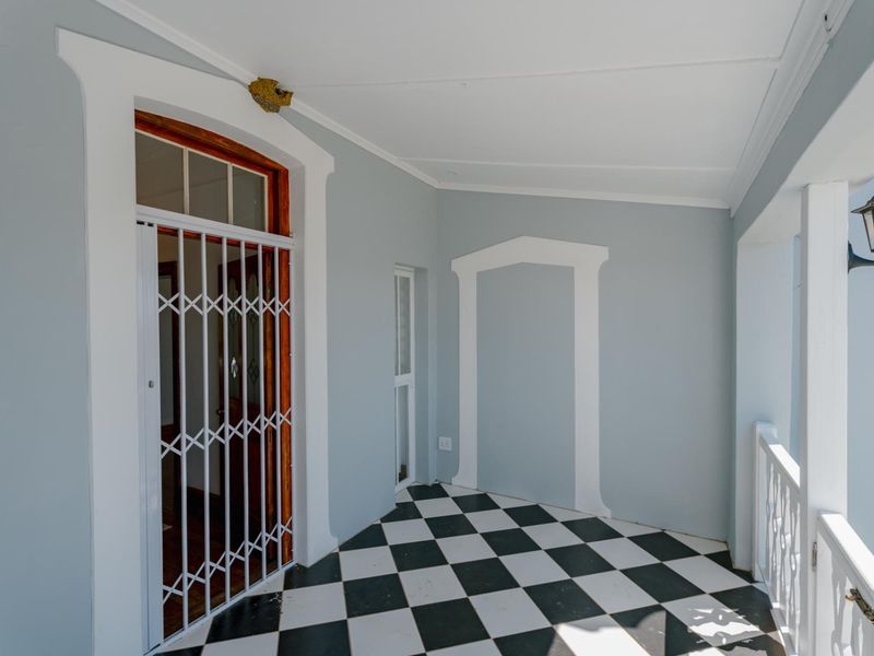A covered patio area featuring classic black and white checkerboard floor tiles, a secure metal gate, and a wall-mounted exterior light fixture.