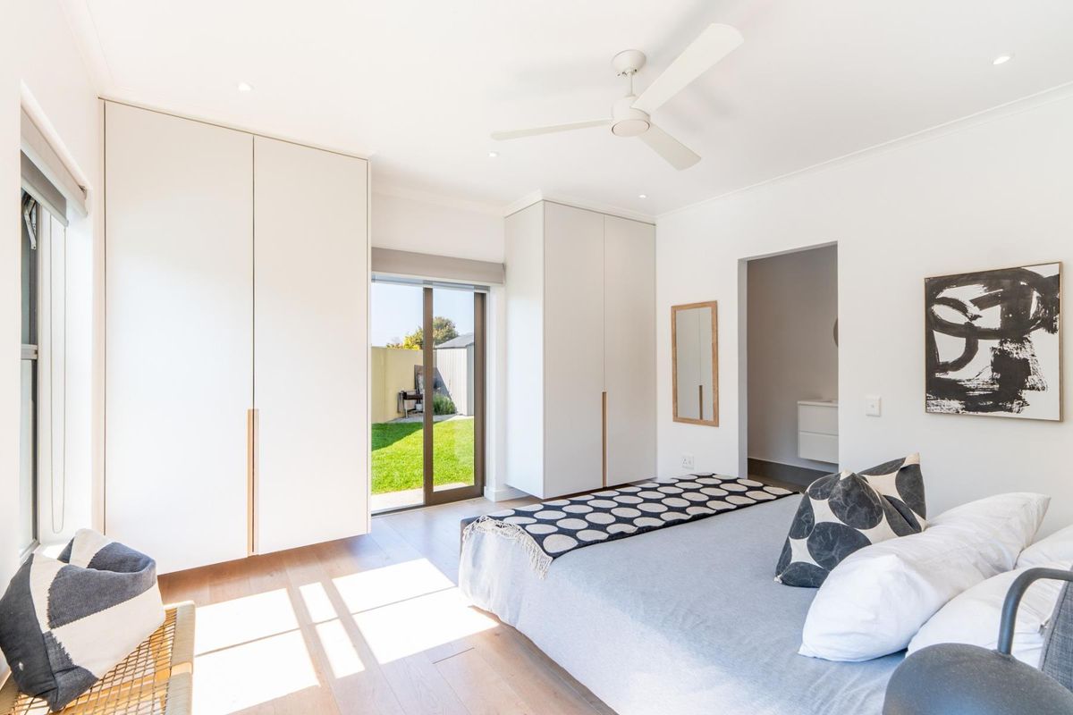 Bright and modern bedroom featuring built-in cupboards, a ceiling fan, timber flooring, and direct access to the rear garden through a sliding glass door.