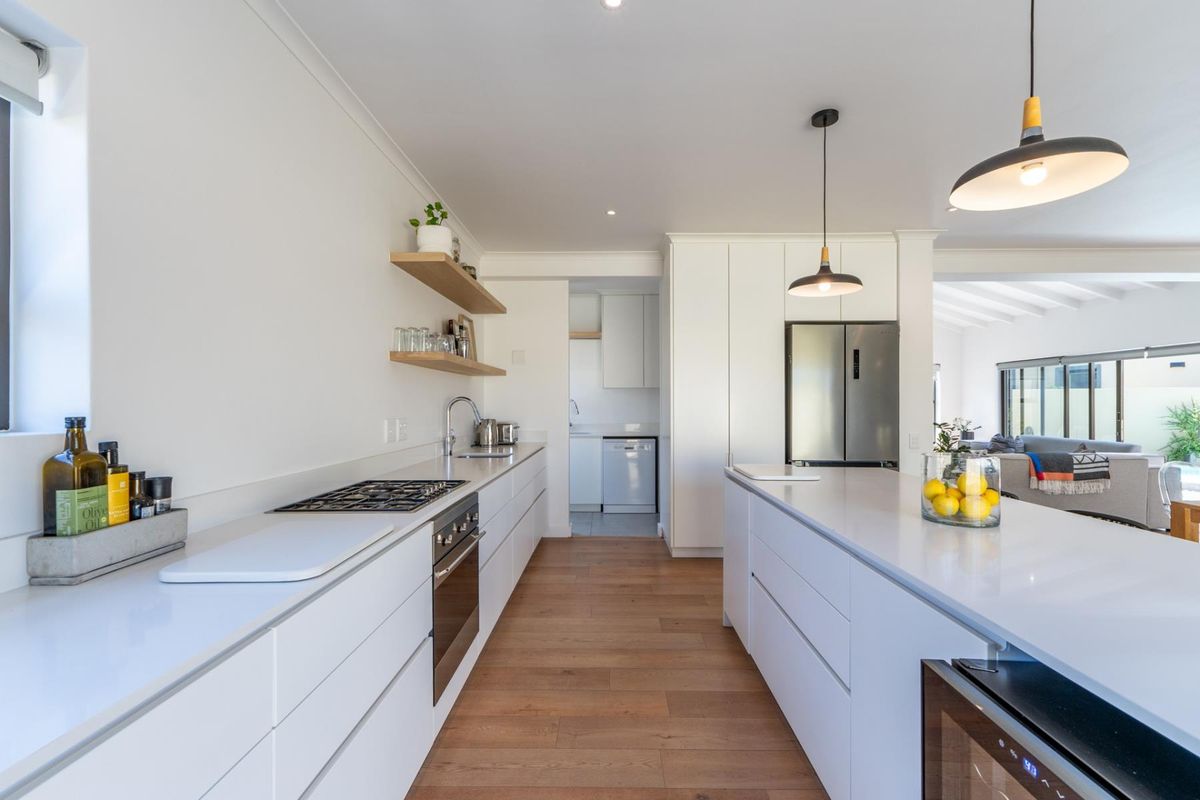 Modern, well-appointed kitchen featuring a large central island, stone countertops, integrated cabinetry, gas cooktop, and warm timber flooring with an adjacent scullery area.