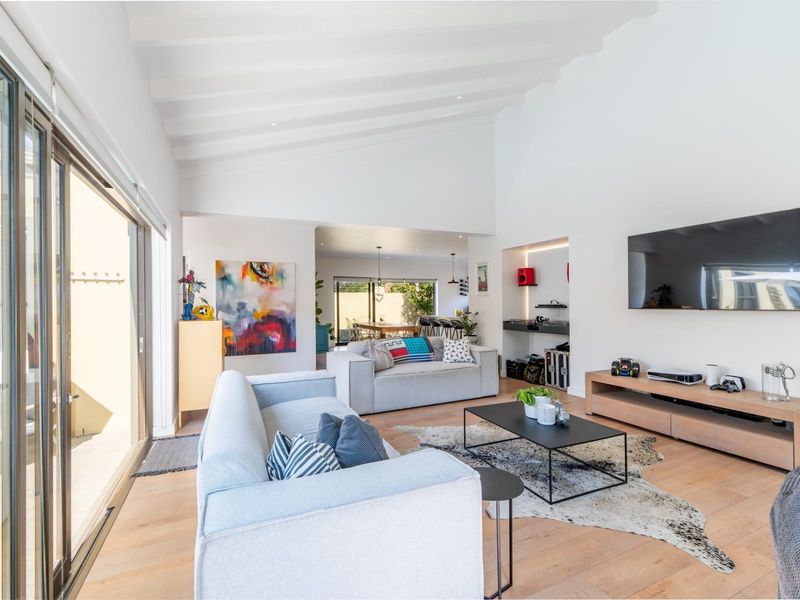 Spacious open-plan living area featuring vaulted ceilings with exposed beams, hardwood flooring, and large sliding glass doors providing seamless access to the outdoors.