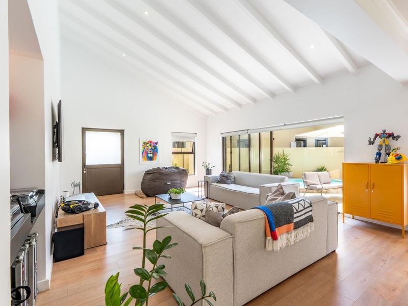 Spacious living room featuring high vaulted ceilings with exposed beams, timber flooring, and large sliding glass doors providing seamless access to the outdoor pool area.