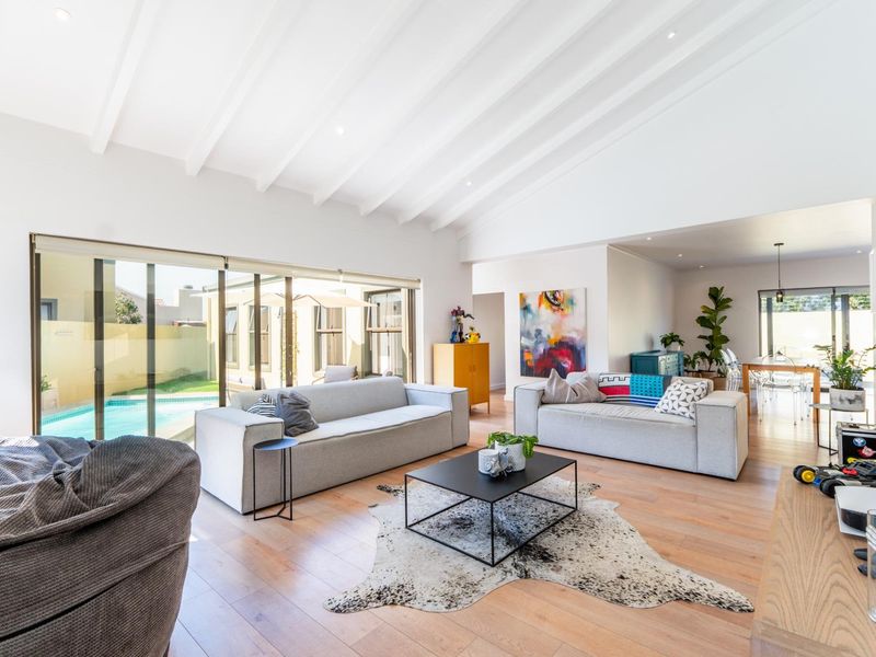 Spacious open-plan living area featuring high exposed beam ceilings, light wood flooring, and large sliding doors providing seamless access to the pool area.