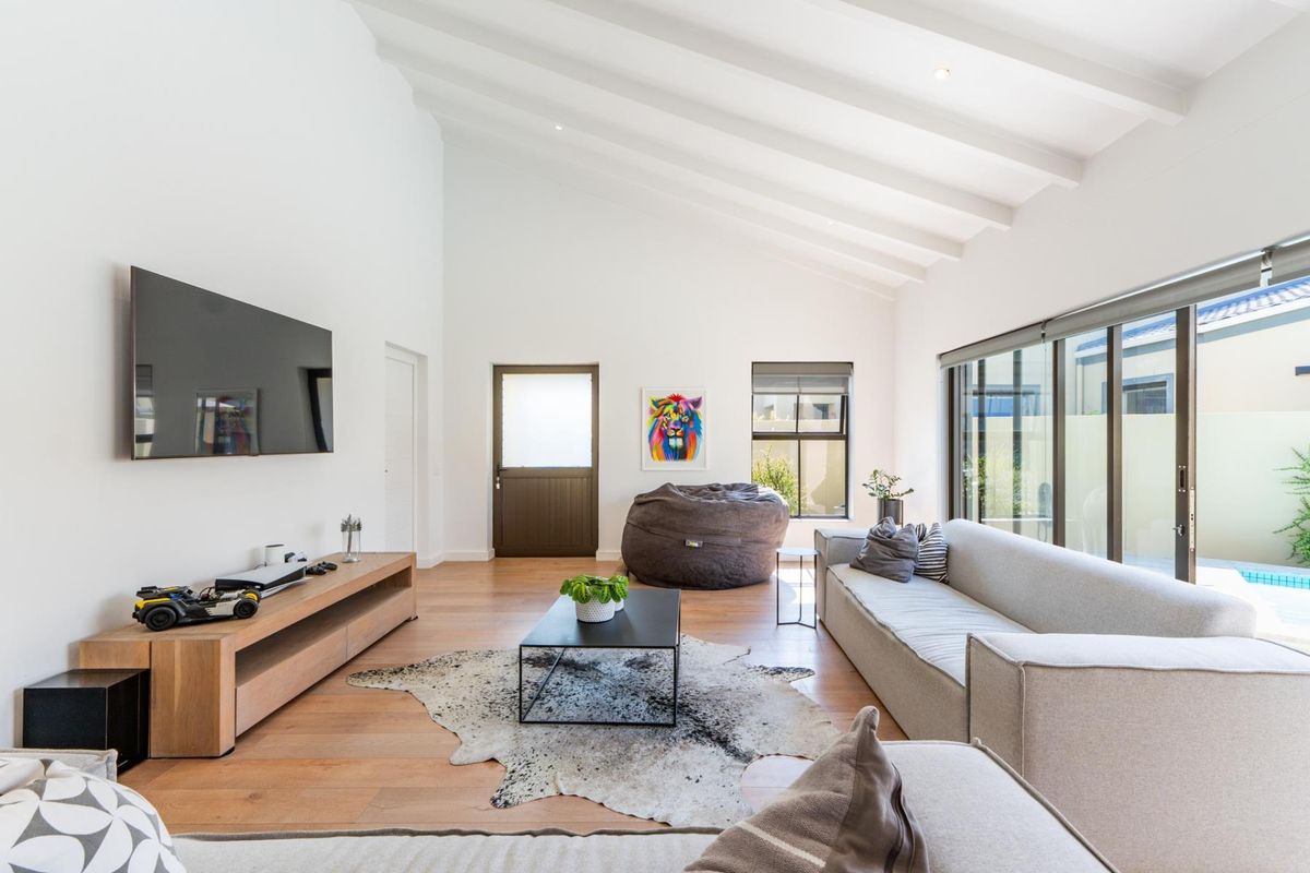 Spacious living room featuring high vaulted ceilings with exposed rafters, timber flooring, and large sliding glass doors providing natural light and pool access.
