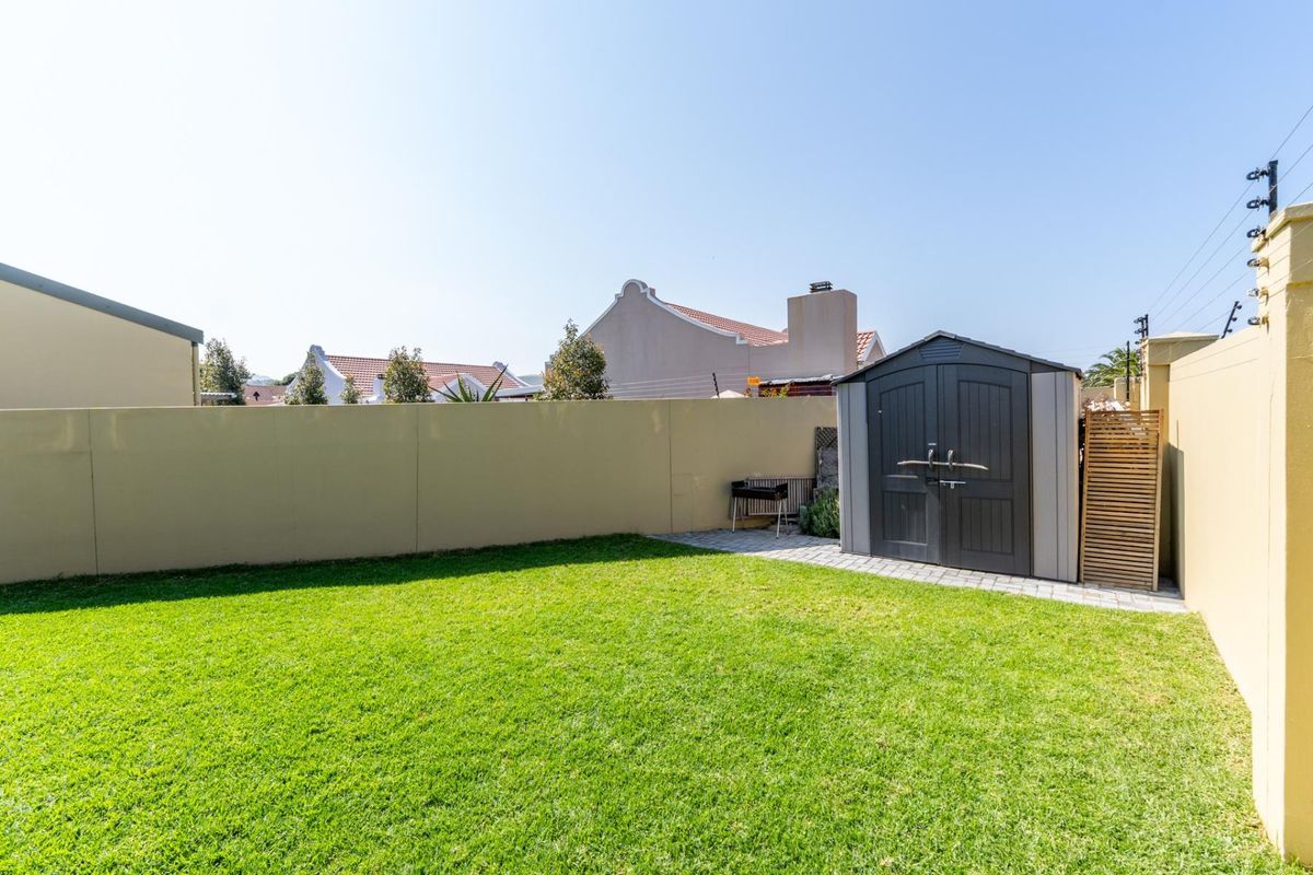 A well-maintained rear garden featuring a manicured lawn, perimeter boundary walls, and a practical storage shed on a paved base.