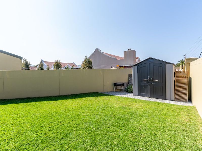 A well-maintained rear garden featuring a manicured lawn, perimeter boundary walls, and a practical storage shed on a paved base.