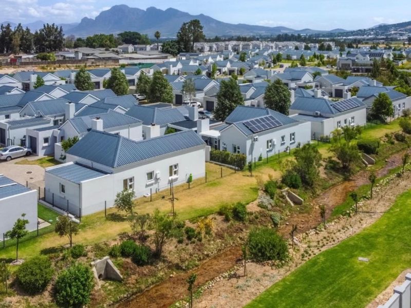 Aerial view of a residential estate featuring modern homes with metal roofs, solar panels, and landscaped surroundings with mountain views.