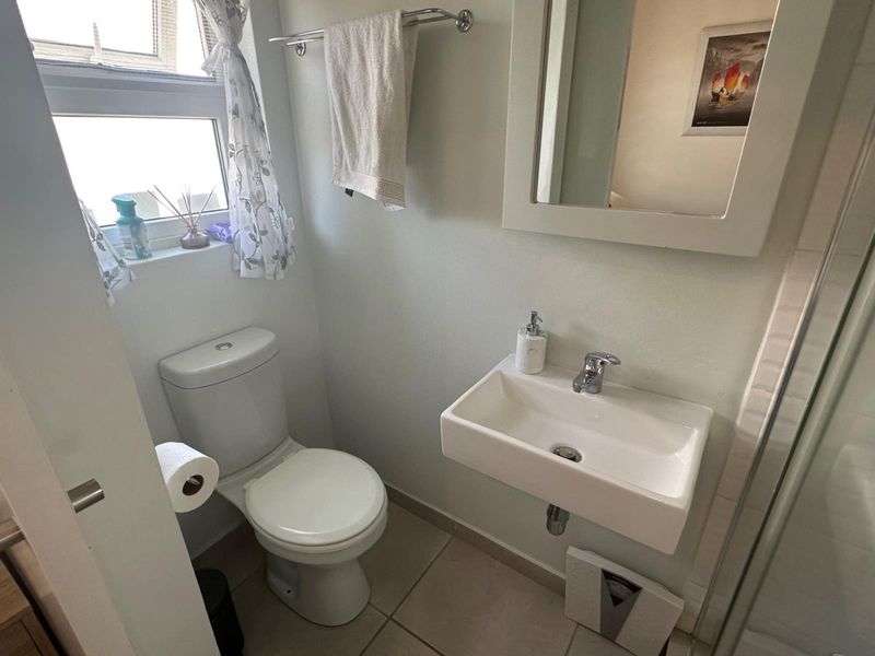 Compact bathroom featuring a wall-mounted basin, toilet, and shower enclosure with tiled flooring and neutral finishes.