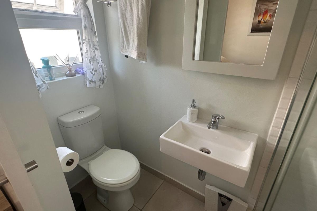 Compact bathroom featuring a wall-mounted basin, toilet, and shower enclosure with tiled flooring and neutral finishes.