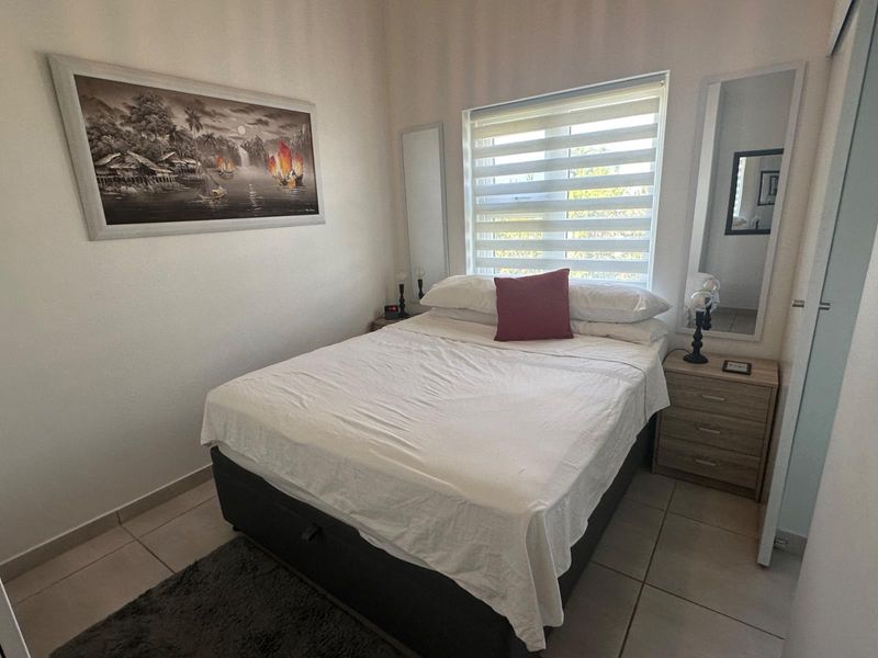 A well-maintained bedroom featuring neutral tiled flooring, a window with modern roller blinds, and built-in wardrobe storage.