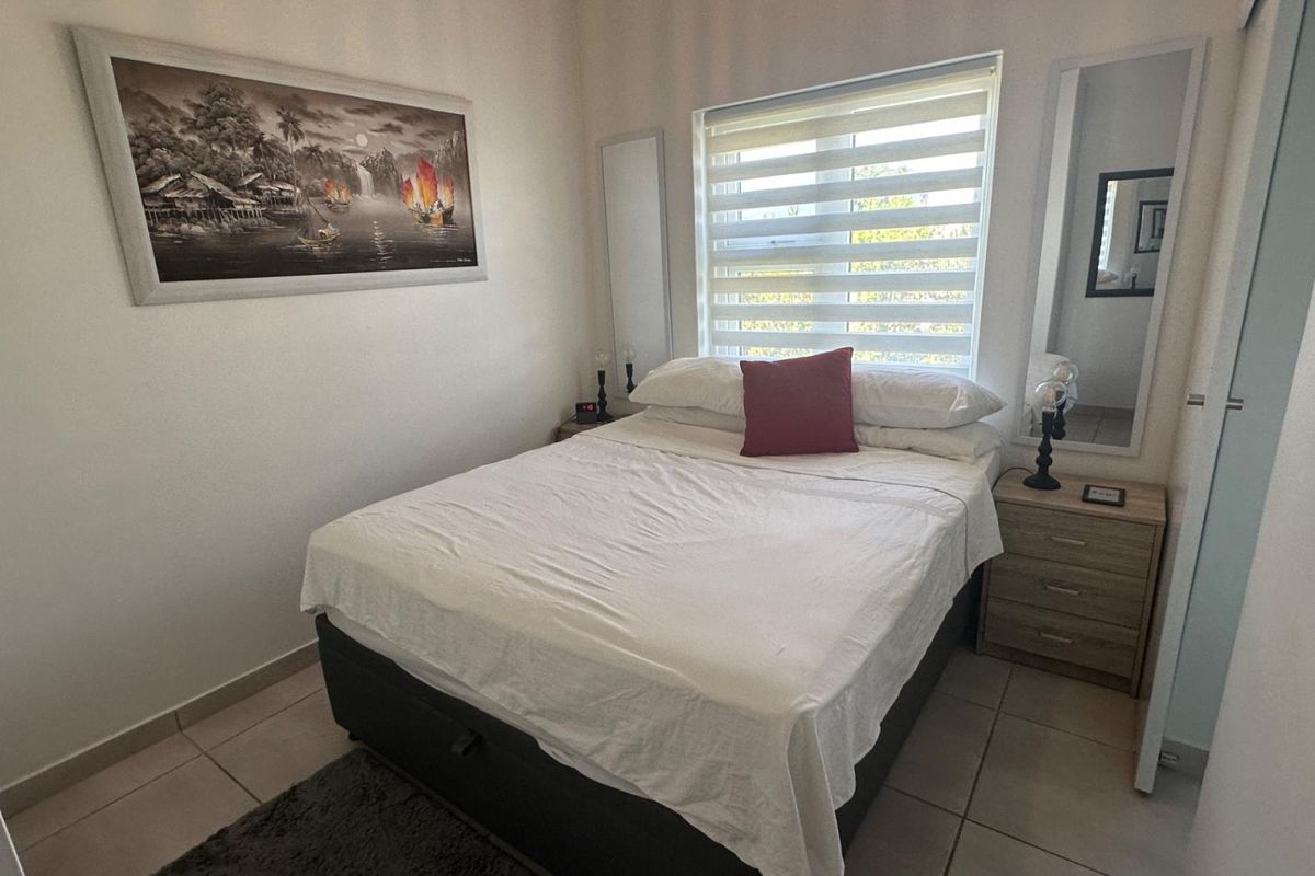 A well-maintained bedroom featuring neutral tiled flooring, a window with modern roller blinds, and built-in wardrobe storage.