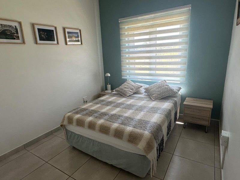 A well-maintained bedroom featuring tiled flooring, a blue accent wall, and modern roller blinds providing natural light.