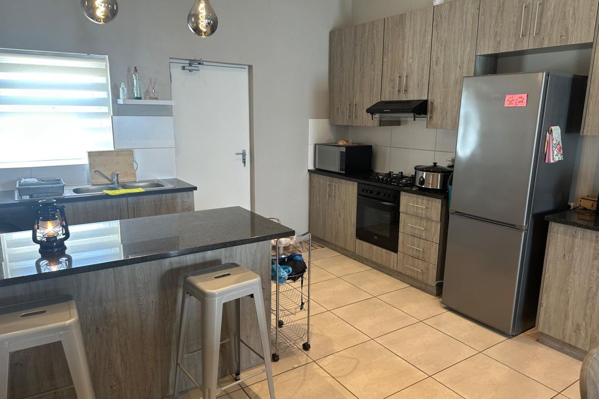 Modern kitchen featuring wood-grain cabinetry, granite countertops, built-in oven with gas hob, extractor fan, and tiled flooring.